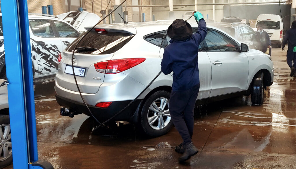 A reliable, customer-focussed team washing a car using a high-pressure washer.
