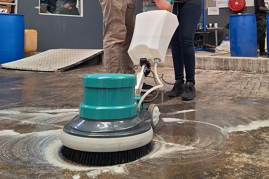 A contract cleaner using a single disc floor scrubber to clean a dirty warehouse floor.