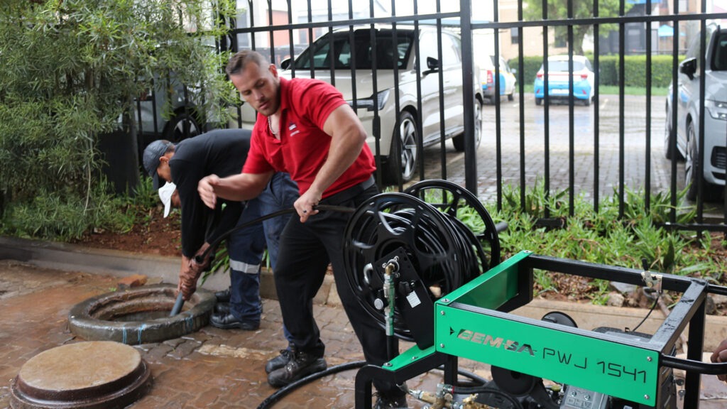 A group of men using a CEMSA Drain Jetting Machine to unclog a sewage drain.
