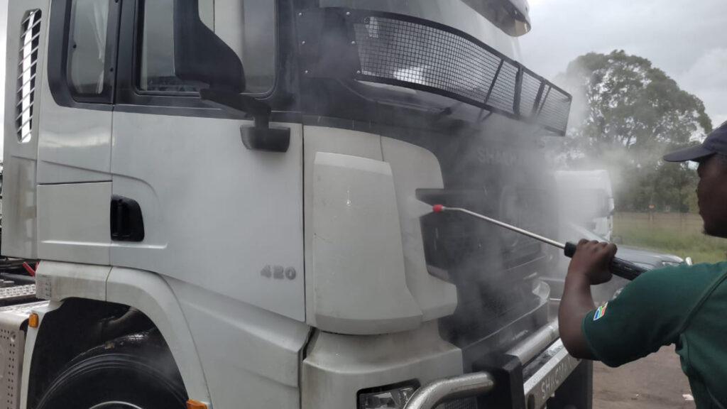 A man using a high-pressure washer to wash a large truck at a truck wash